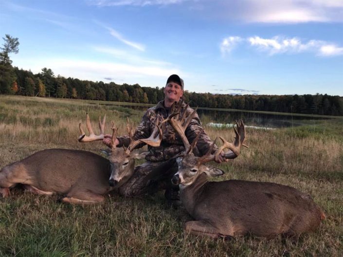 a man posses with two whitetail bucks 
