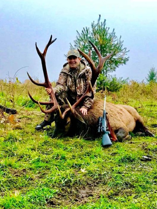 A person posing with a downed elk 