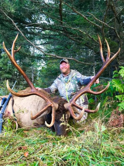 a man posing with a  trophy elk with a very large rack 