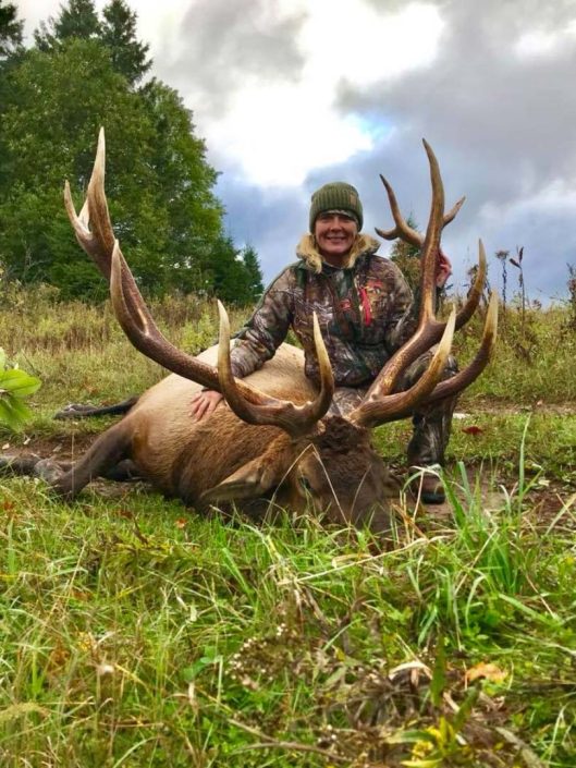 A woman poses with a downed trophy elk 