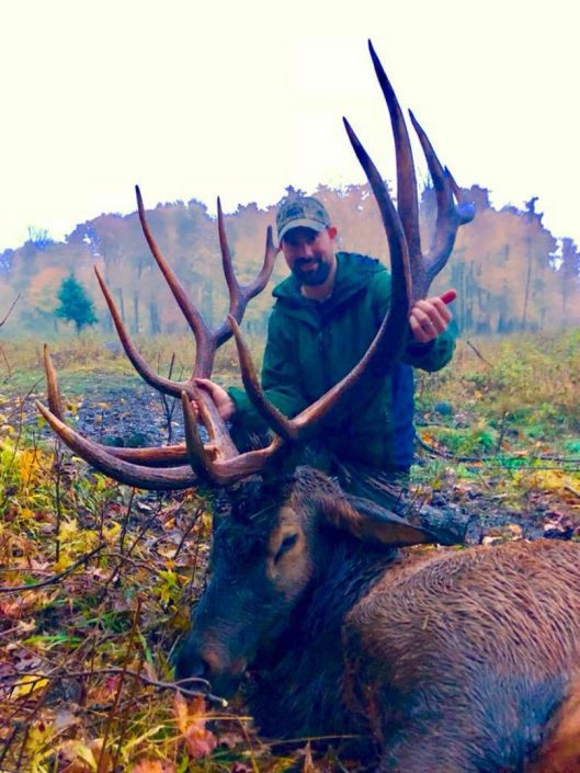 A man holds up large elk antlers 