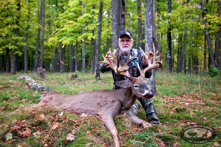 a man holds up the large antlers on his trophy buck 
