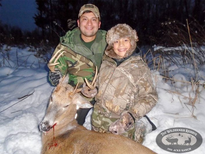 Two hunters hold up their whitetail kill 