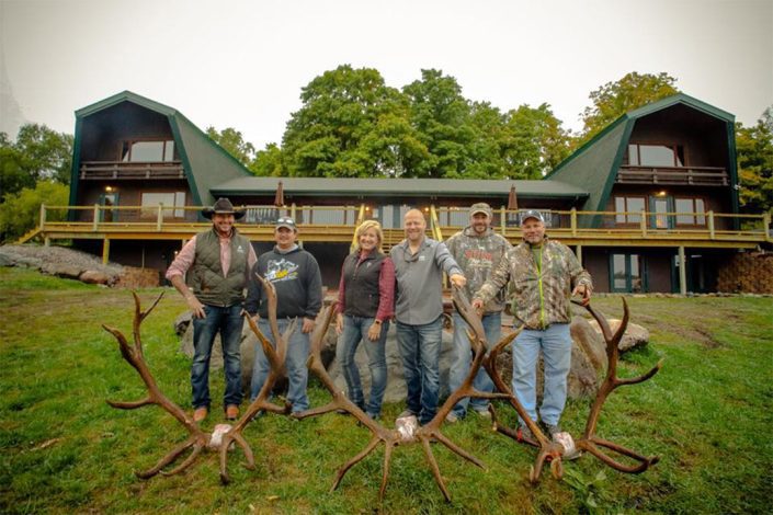 a group poses with three sets of elk antlers in front of the lodge 