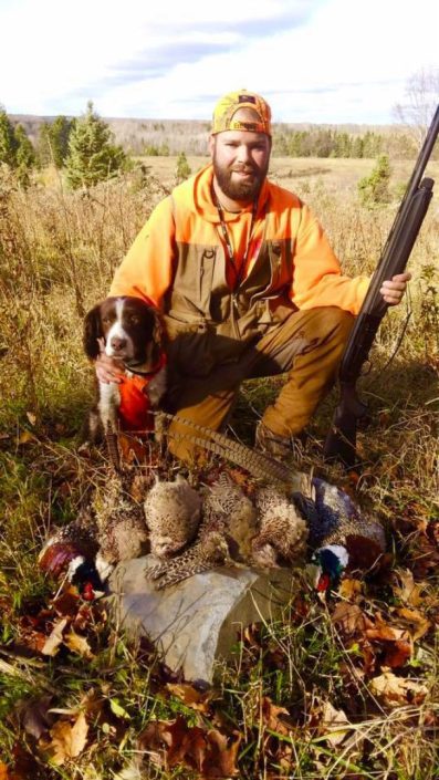 A man and a hunting dog show off their pheasant kills 