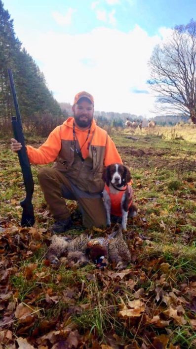 A man poses with a hunting dog and some pheasants 