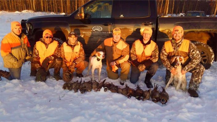 a group poses with their waterfowl trophies and two hunting dogs