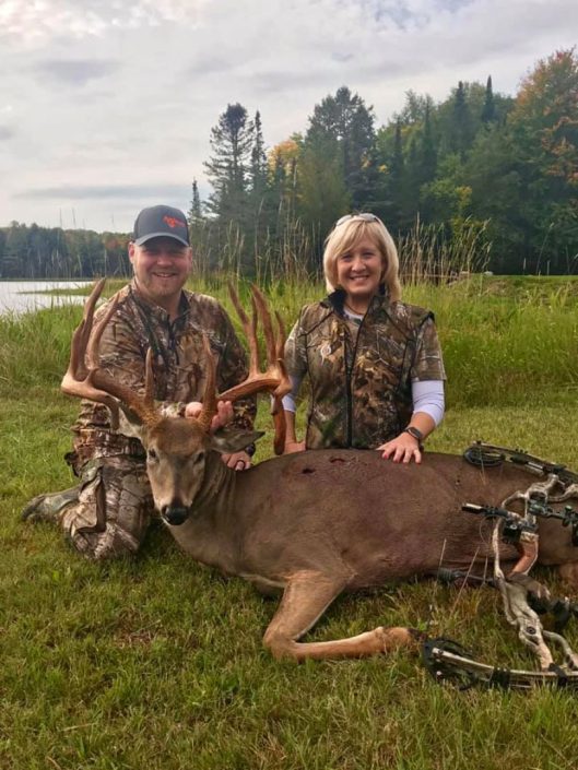 a couple pose with a whitetail they have killed, and a compound bow