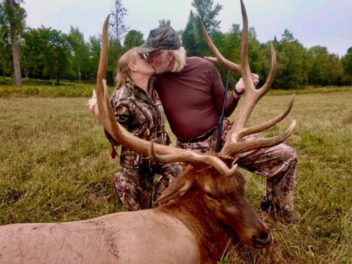 a couple kiss while showing the elk they have hunted 
